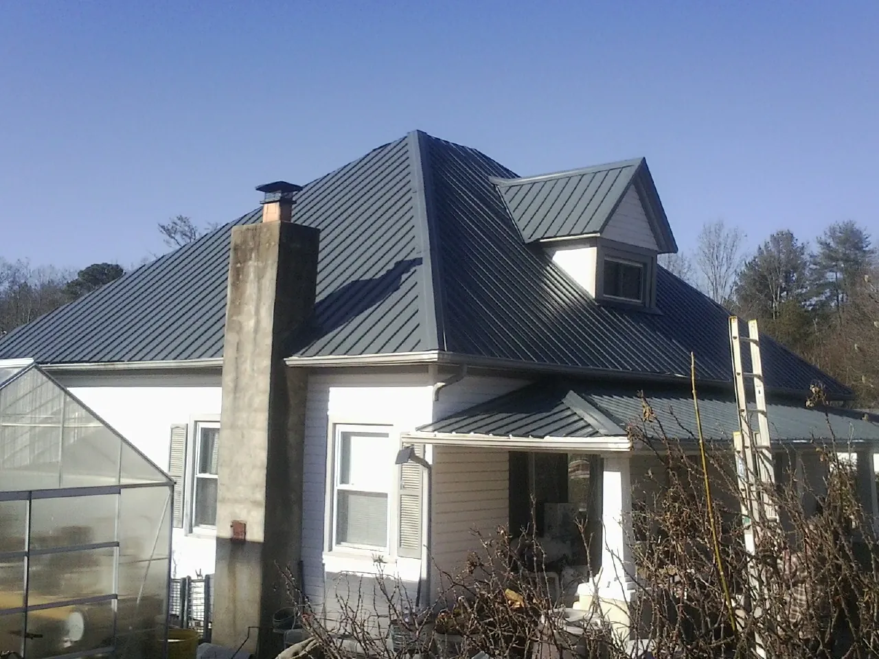 Dark blue standing seam metal roof on a white farmhouse with dormer — Slate & Tile Roof Repair by Roofing Brothers in Pulaski