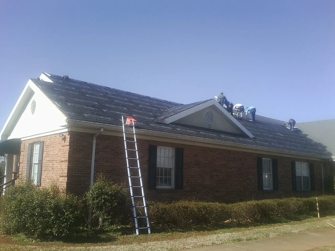 Crew tearing shingles off a brick ranch roof with a ladder set — Emergency Roof Repair work by our crew in Pulaski