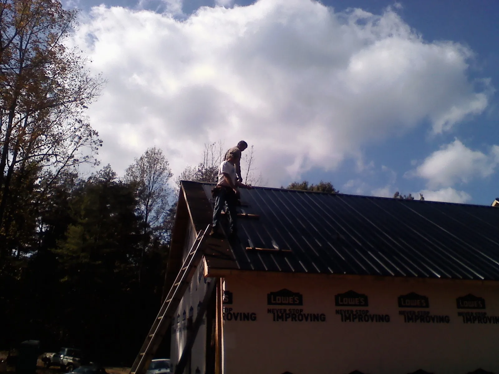 Roofer fastening dark metal panels high against a cloudy sky, from a Roof Inspection job in Pulaski